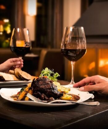 Two individuals in bathrobes share a joyful moment, raising wine glasses and indulging in tasty dishes. - Hausion